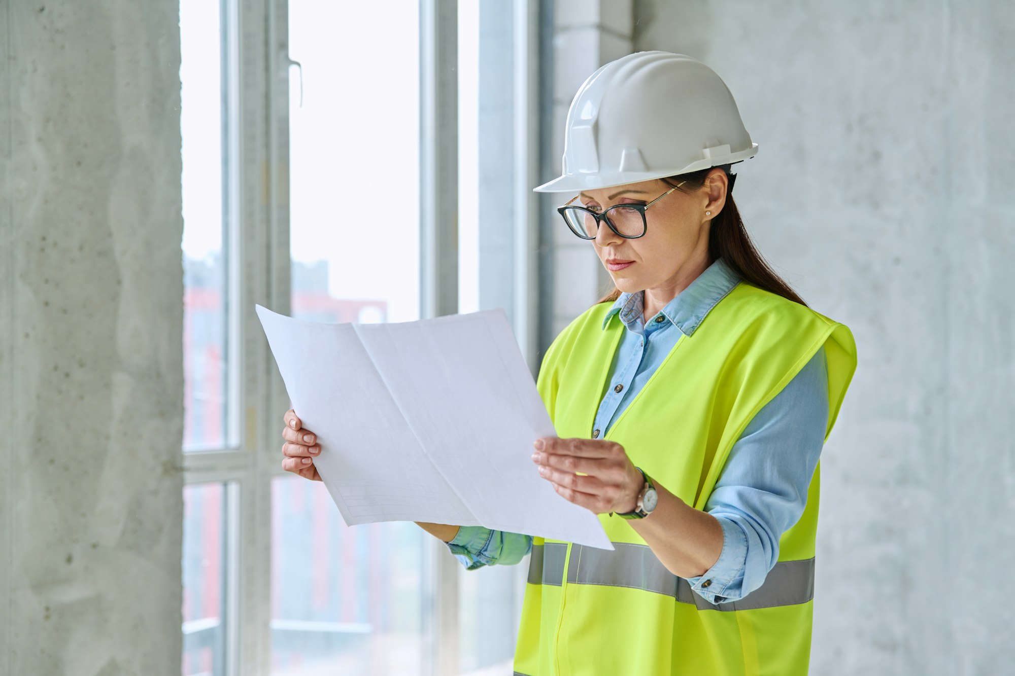 Technical profession woman in protective vest helmet working on construction